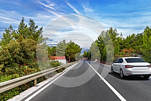 A white sedan drives down a peaceful forested highway photo