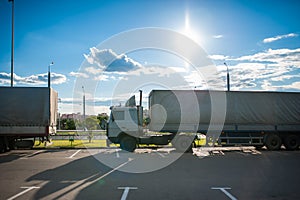 A white semi truck with a cargo trailer rides into the parking lot and parked with other vehicles. Wagons on unloading goods