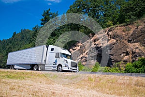 White semi truck trailer going highway with rocks green trees