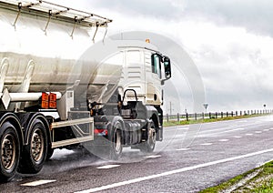 A white semitrailer tractor with a stainless tanker truck transports dangerous goods on the road. Kotsnet transportation