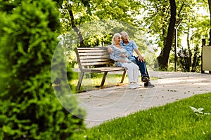 White senior couple hugging and smiling while sitting on bench