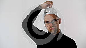 White serious attractive man in glasses puts a tinfoil helmet to the brains on his head. Emotional handsome guy with glasses.