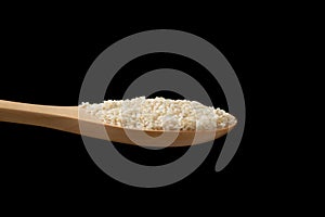 White sesame seeds in wooden spoon on black background