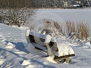 White shades of winter, a snow-covered bench by a frozen pond