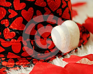 White shag carpet, one white pillow heart, rose petals, black hat with many red hearts