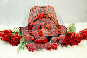 On white shag carpet... Valentines black hat, with red hearts, on top of dozen small red roses,