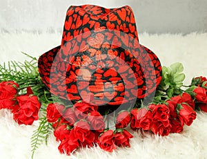 On white shag carpet... Valentines black hat, with red hearts, on top of dozen small red roses,