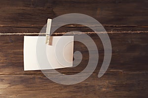 A white sheet of paper hanging on clothespin, place for text, on a background of old wooden