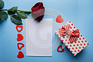 White sheet of paper for message to a loved one on a blue background with shiny hearts, gift box and rose