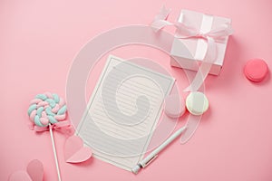 A white sheet of paper for message to loved one, gift box, macaron, candy on pink background. Happy womans day concept. Mock up