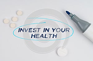 On a white sheet of paper, tablets, a marker and an inscription - INVEST IN YOUR HEALTH indicated by a drawn oval