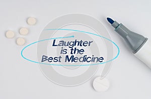 On a white sheet of paper, tablets, a marker and an inscription Laughter is the Best Medicine indicated by a drawn oval