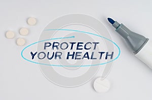 On a white sheet of paper, tablets, a marker and an inscription - PROTECT YOUR HEALTH indicated by a drawn oval