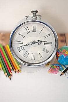 A white sheet surrounded by colors pencils, a clock, clips and a world map