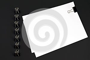 White sheets and binder clip on black background, top view, mockup.