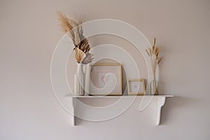 White shelf with easels and dry flowers and mock up frames with drawings