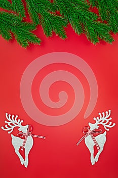 White shiny deer on red background with green branches of Christmas tree. New Year