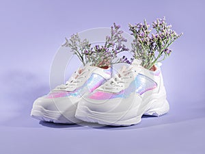 White shiny sneakers with flowers inside on purple background