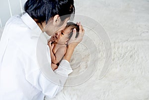 White shirt Asian mother is kissing and holding newborn baby near fluffy bed with concept love and careful for baby