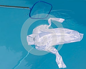 A white shirt floats on the water of a swimming pool, while someone tries to fish it with a net