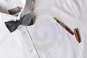 White shirt with grey bow tie, blank paper business card and stylish pen.Empty space