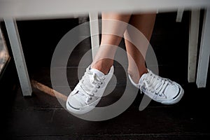 White shoes,Fashion woman`s legs with sneakers seated on Wooden