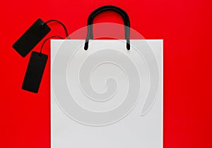 White shopping bag with black price tags on red background.