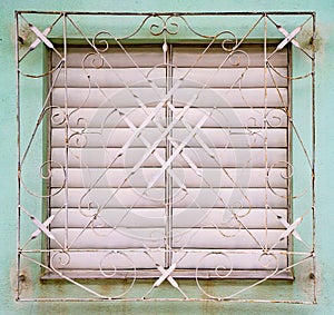 White shutters closed on window behind white metal grill on fade