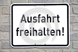 A white sign on a brick wall, with the words `Ausfahrt freihalten`, translation: keep gateway clear