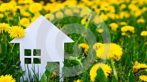 White silhouette of a toy house cut out of cardboard on a background of dandelions. Copy space