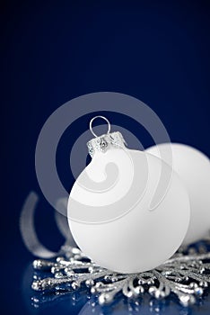 White and silver christmas ornaments on dark blue background with space for text.