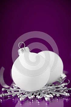 White and silver christmas ornaments on dark purple background with space for text.