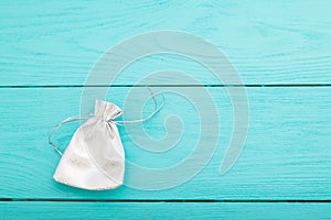 White silver drawstring bag on blue wooden background. Fabric cotton small bag. Jewelry pouch. Top view. Copy space and mock up.