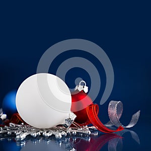 White, silver and red christmas ornaments on dark blue background with space for text.