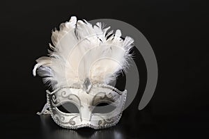 White and silver venetian carnival mask with feathers on a black background