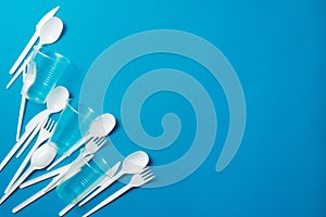 White single-use plastic knives, spoons, forks on a blue background. Say no to single use plastic. Environmental, pollution