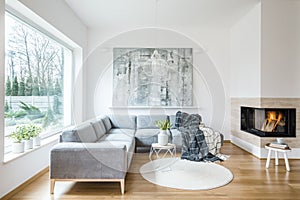 White sitting room interior with corner grey sofa, tulips in vase placed on end table, fireplace and modern art painting