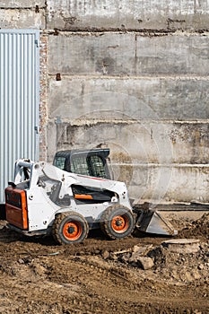 White skid steer loader at a construction site working with a soil. Industrial machinery. Industry.