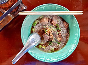White slim noodle soup with meatball and pork stewed served in a green bowl.