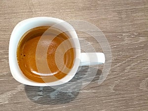 A white small cup of hot espresso coffee on wooden table top view