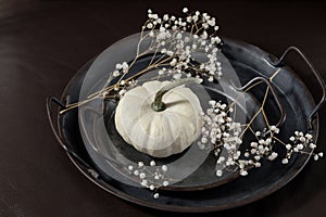 White small pumpkin with dried flowers on dark retro metallic plate or tray on brown leather couch. Holiday autumn composition in