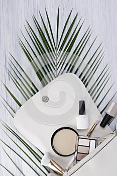 White small women`s handbag and makeup cosmetics are on the background of a green twig