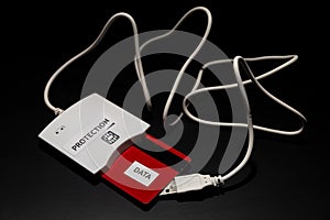 White smart card reader with white wire and with red card in the reader are on the black background/table. Note `Protection` is on