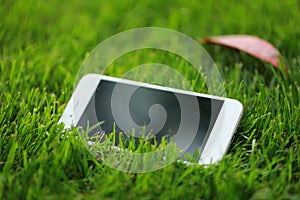 A white smart phone cellphone on green grass lawn in summer spring park garden at sunny day