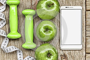 White smartphone, dumbbells and green ripe apple. Concept: healthy lifestyle. on a gray wooden background