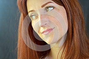 White smiling girl with red hair and green eyes with eyelash extensions on a dark background looks right