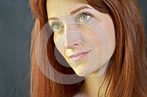 White smiling girl with red hair and green eyes with eyelash extensions on gray background looking up