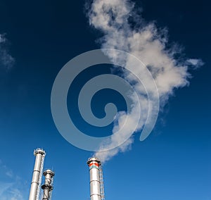 White smoke from coal powered plant stacks, profiled on bright blue sky