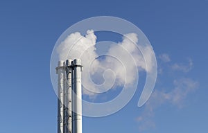 White smoke comes from a white chimney pipe on a background of blue sky.