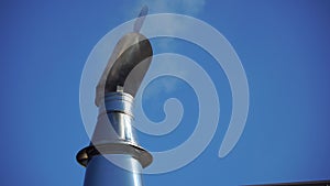 White smoke flies from Stainless Steel Wind Directional Cowl on Chimney Rotating Gently on Wind. Flue pipe for the stove